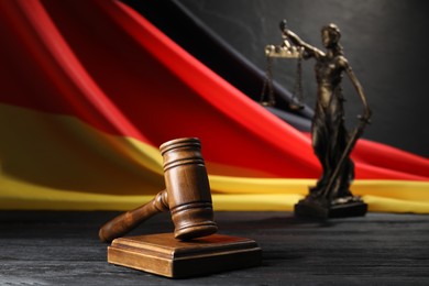 Photo of Judge's gavel, flag of Germany and statue of Lady Justice on black wooden table, closeup