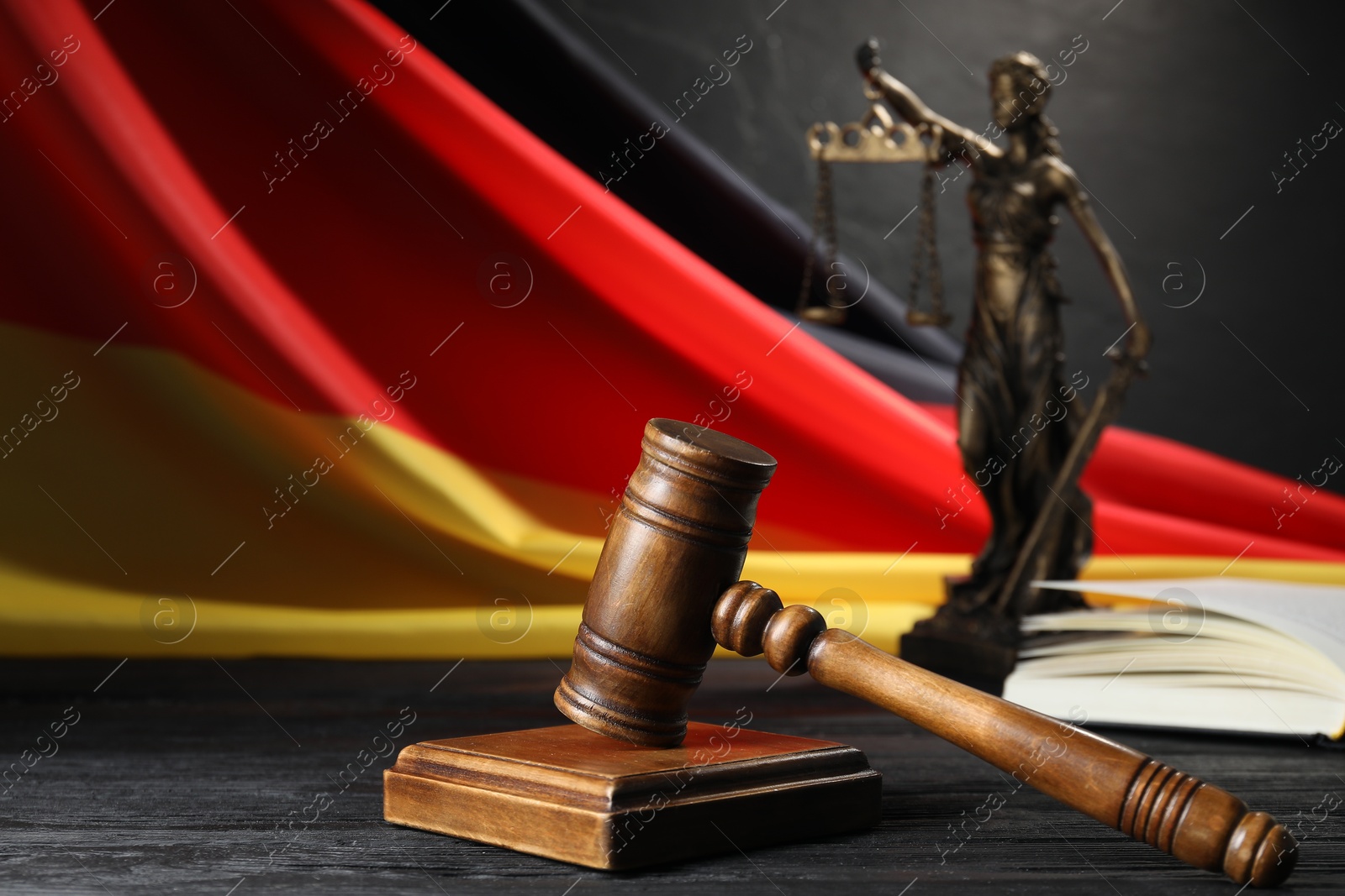 Photo of Judge's gavel, book, flag of Germany and statue of Lady Justice on black wooden table, closeup