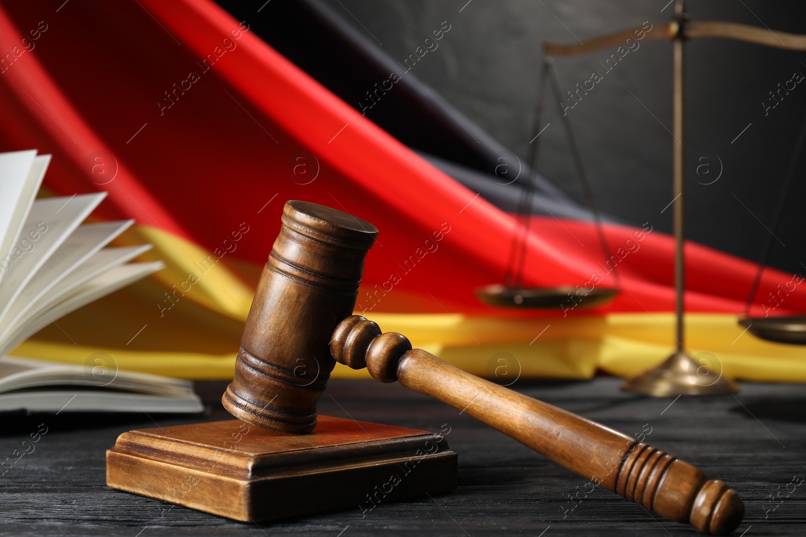 Photo of Judge's gavel, book, flag of Germany and scales on black wooden table, closeup