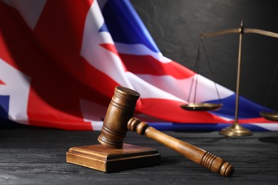 Photo of Judge's gavel, flag of United Kingdom and scales on black wooden table, closeup
