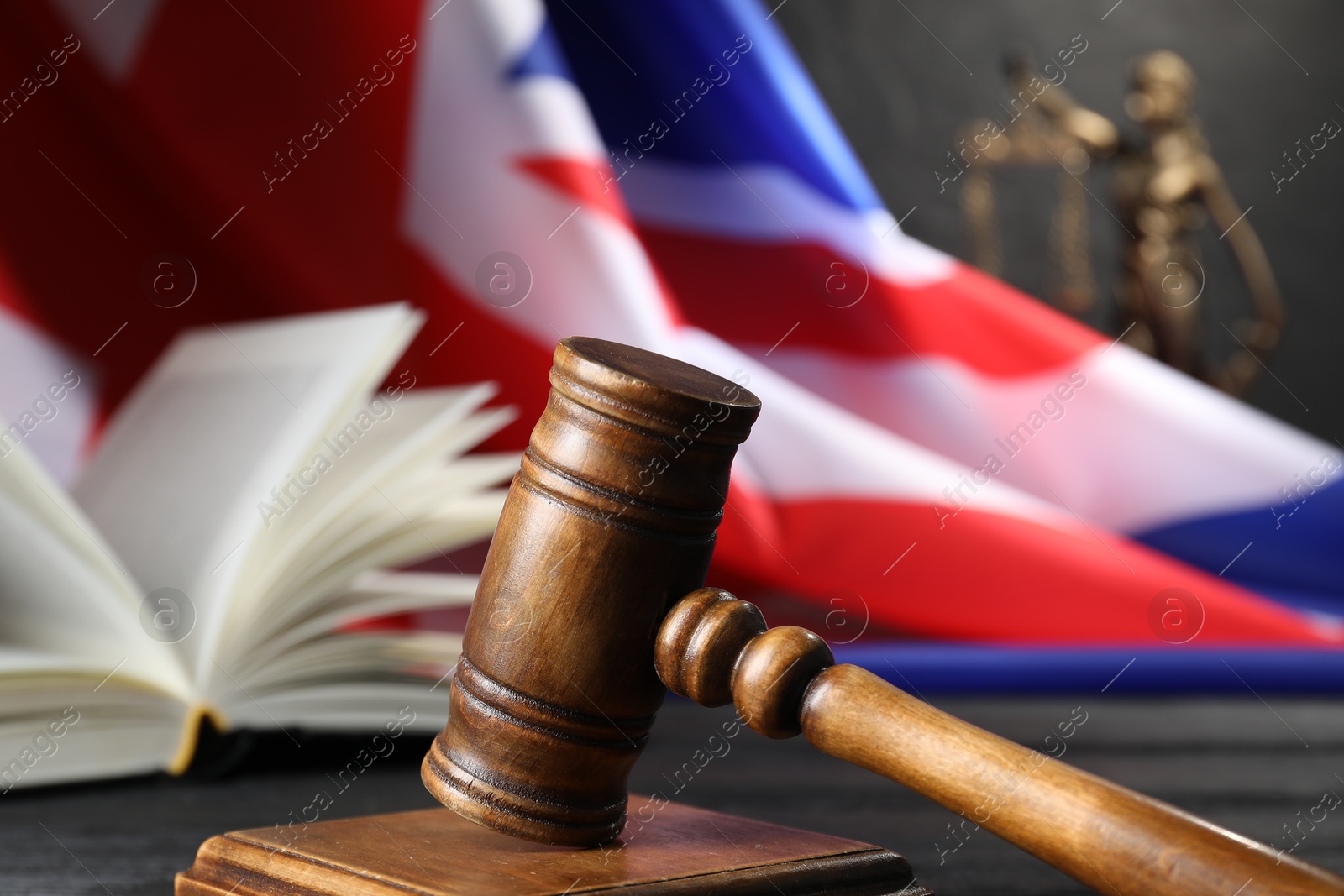 Photo of Judge's gavel, book, flag of United Kingdom and statue of Lady Justice on table, closeup