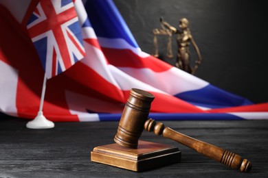 Photo of Judge's gavel, flags of United Kingdom and statue of Lady Justice on black wooden table, closeup
