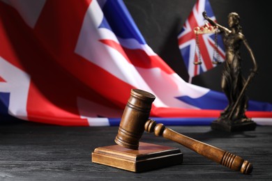 Photo of Judge's gavel, flags of United Kingdom and statue of Lady Justice on black wooden table, closeup