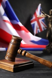 Photo of Judge's gavel, flags of United Kingdom and statue of Lady Justice on black wooden table, closeup