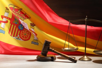Photo of Judge's gavel and scales on wooden table against flag of Spain