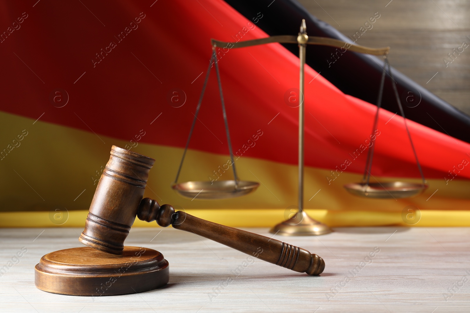 Photo of Judge's gavel and scales on wooden table against flag of Germany