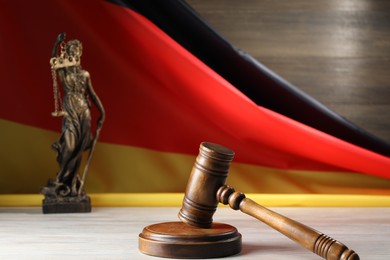 Photo of Judge's gavel and statue of Lady Justice on wooden table against flag of Germany, closeup