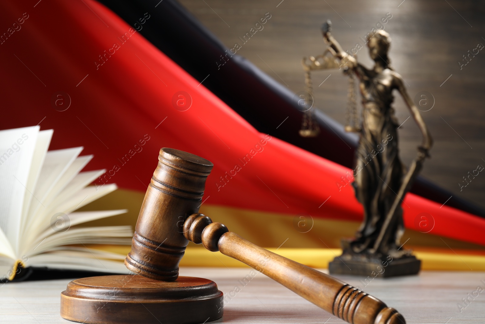 Photo of Judge's gavel, book and statue of Lady Justice on wooden table against flag of Germany, closeup