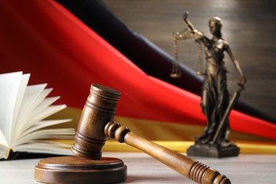 Photo of Judge's gavel, book and statue of Lady Justice on wooden table against flag of Germany, closeup