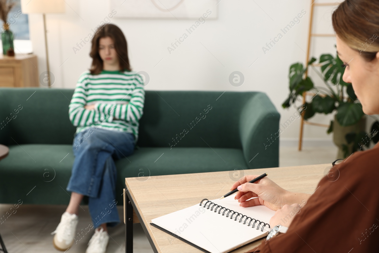 Photo of Professional psychologist working with teenage girl and writing in notebook in office, selective focus