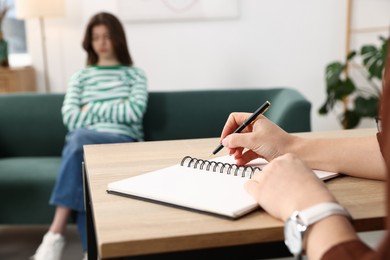 Photo of Professional psychologist working with teenage girl and writing in notebook in office, selective focus