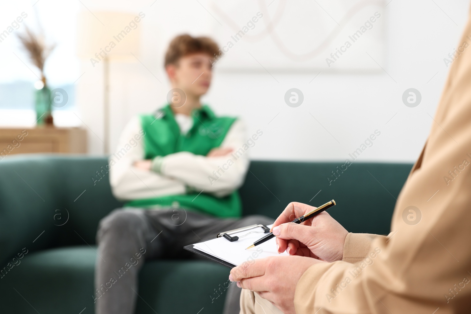 Photo of Professional psychologist with clipboard working with teenage boy in office, selective focus