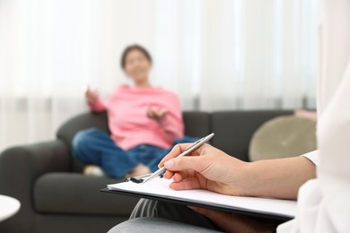 Photo of Professional psychologist working with teenage girl and writing in clipboard in office, selective focus