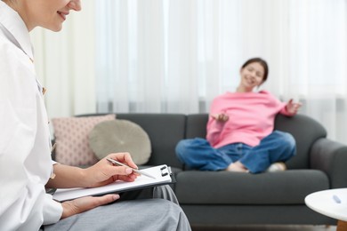 Photo of Professional psychologist working with teenage girl and writing in clipboard in office, selective focus