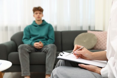 Photo of Professional psychologist working with teenage boy and writing in clipboard in office, selective focus
