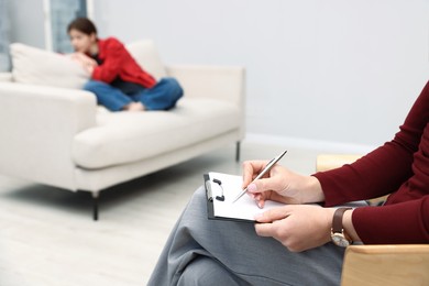 Photo of Professional psychologist working with teenage girl and writing in clipboard in office, selective focus