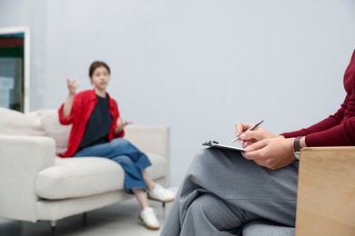 Photo of Professional psychologist working with teenage girl and writing in clipboard in office, selective focus