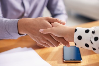 Photo of Man and woman shaking hands at wooden desk indoors, closeup