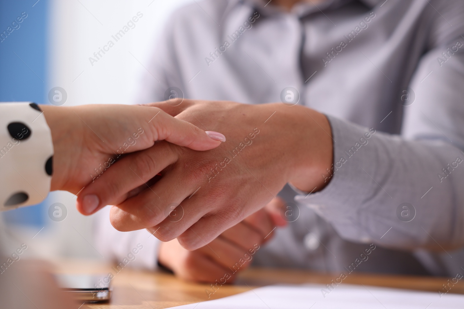Photo of Man and woman shaking hands at wooden desk indoors, closeup