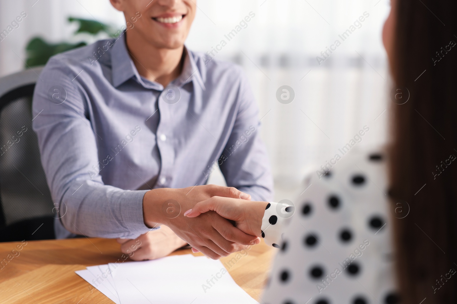 Photo of Man and woman shaking hands at wooden desk indoors, closeup