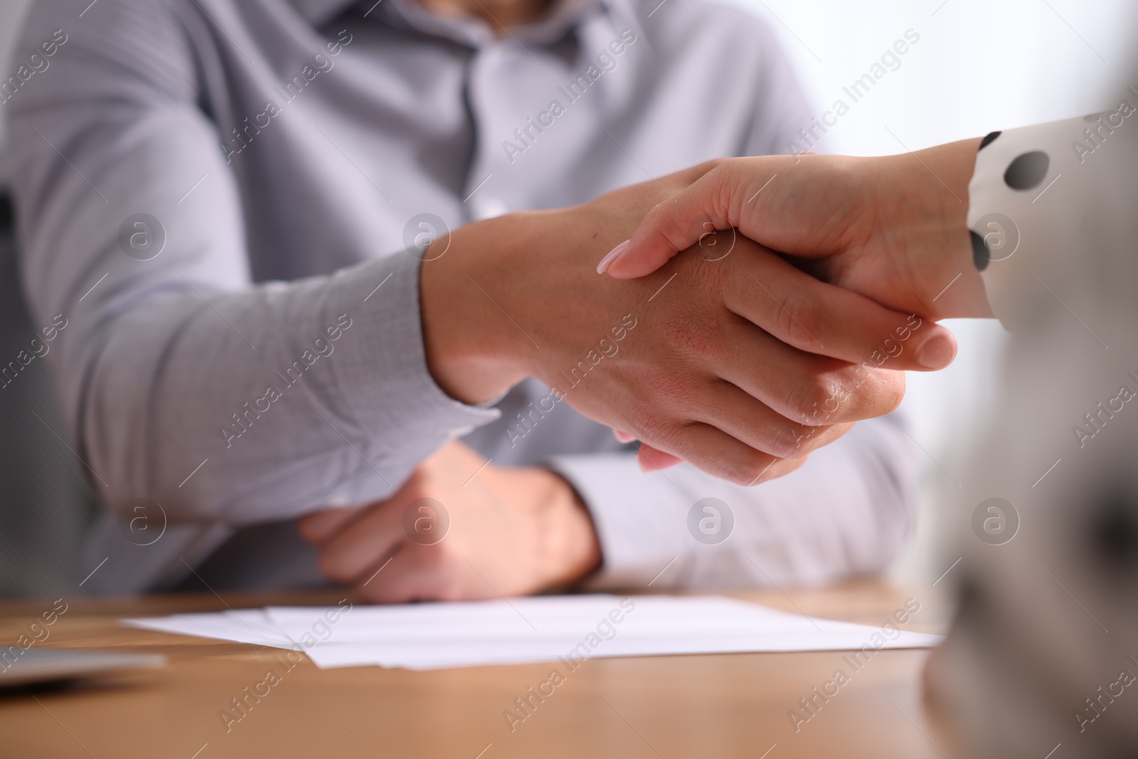 Photo of Man and woman shaking hands at wooden desk indoors, closeup