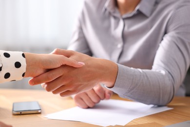 Photo of Man and woman shaking hands at wooden desk indoors, closeup