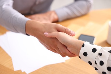 Photo of Man and woman shaking hands at wooden desk indoors, closeup