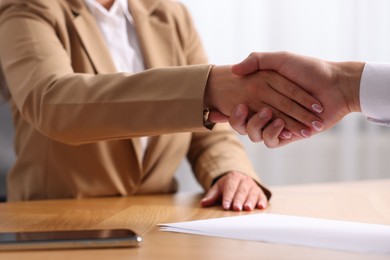 Photo of Man and woman shaking hands at wooden desk indoors, closeup