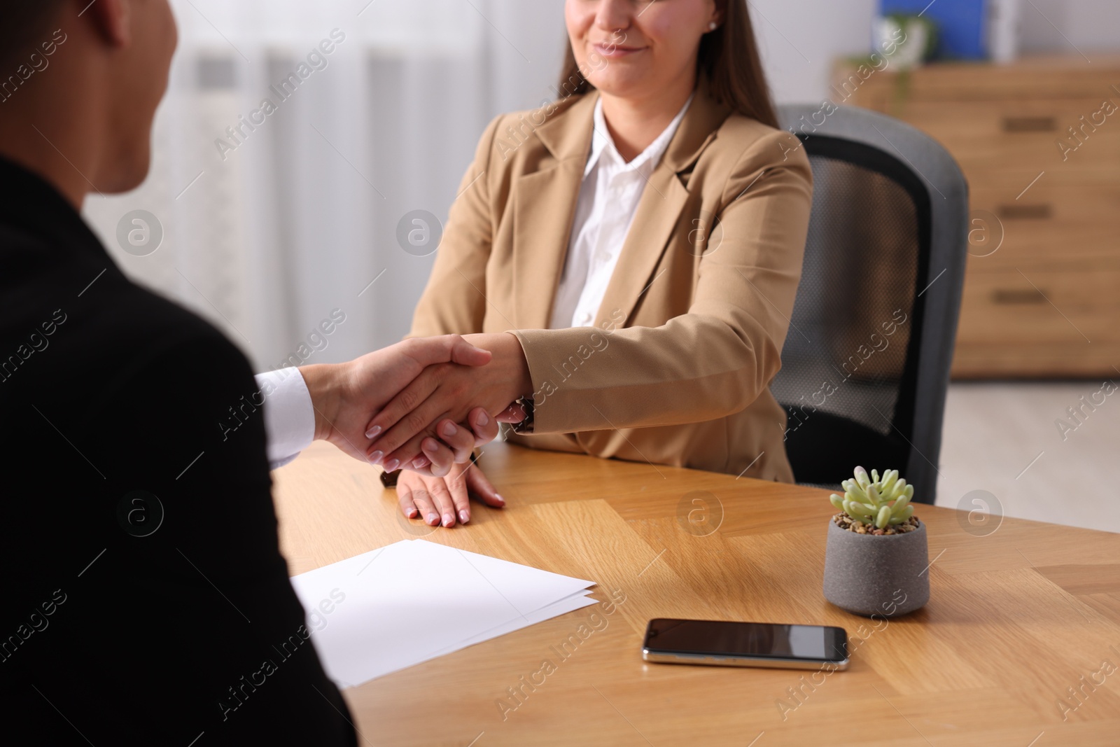 Photo of Man and woman shaking hands at wooden desk indoors, closeup
