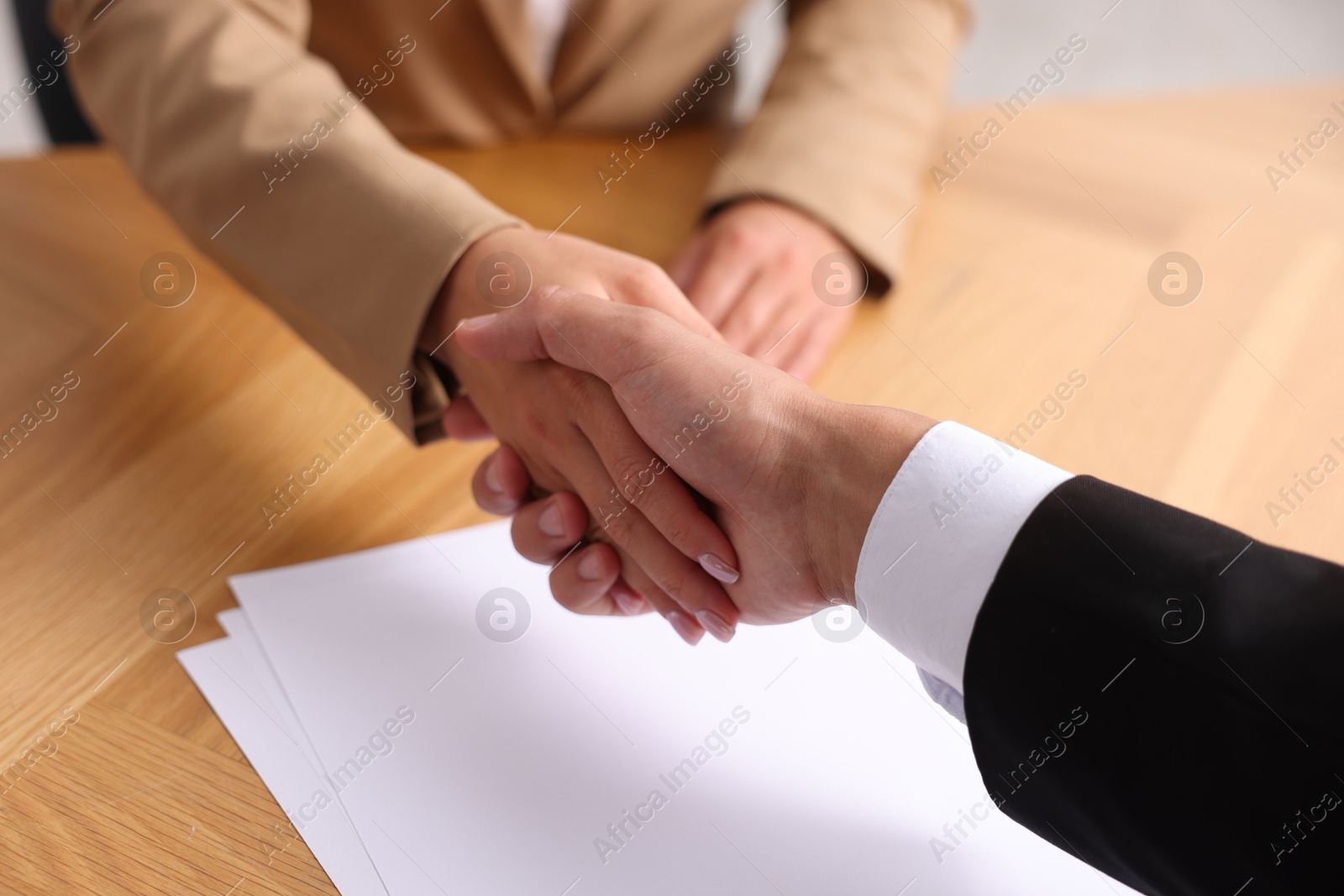 Photo of Man and woman shaking hands at wooden desk indoors, closeup