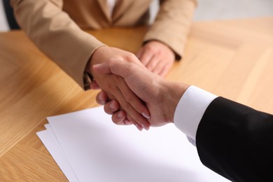 Photo of Man and woman shaking hands at wooden desk indoors, closeup