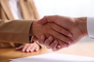 Photo of Man and woman shaking hands at wooden desk indoors, closeup