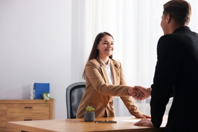 Photo of Man and woman shaking hands at wooden desk in office. Space for text