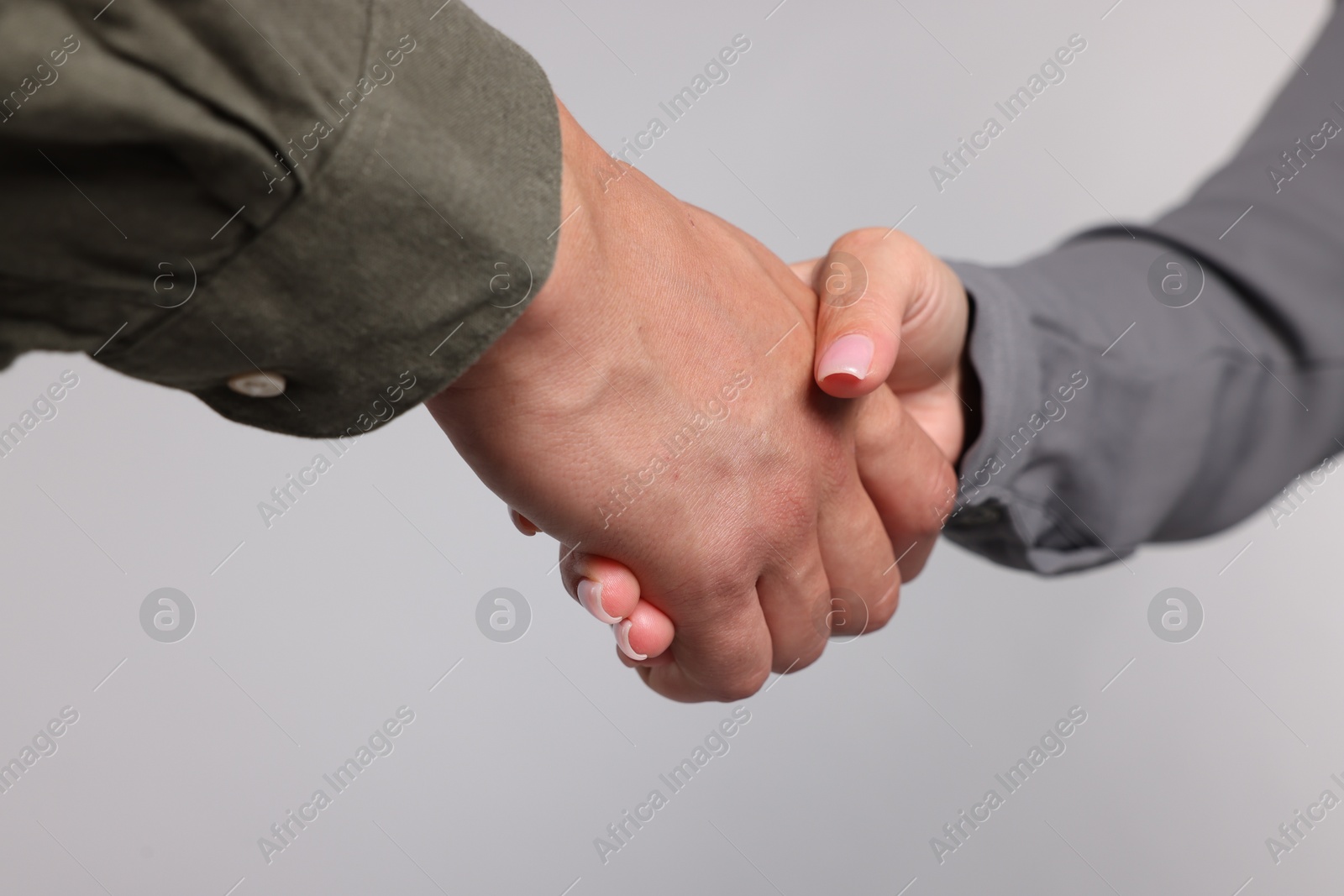 Woman and man shaking hands on light grey background, closeup Photo of Woman and man shaking hands on light grey background, closeup