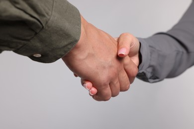Photo of Woman and man shaking hands on light grey background, closeup