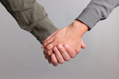 Photo of Woman and man holding hands on light grey background, closeup