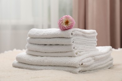 Photo of Stack of white terry towels and dahlia flower on bed indoors, closeup