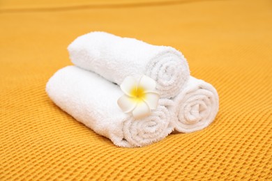 Photo of Rolled terry towels and plumeria flower on yellow blanket, closeup
