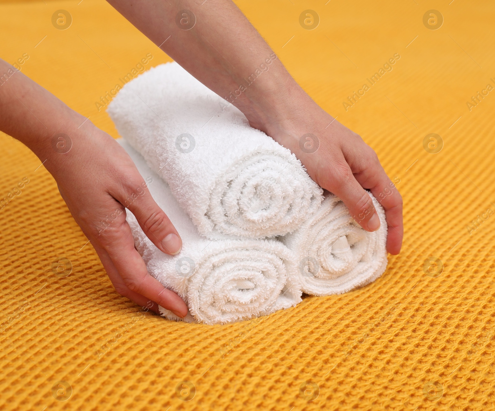 Photo of Woman putting rolled terry towels onto yellow blanket, closeup