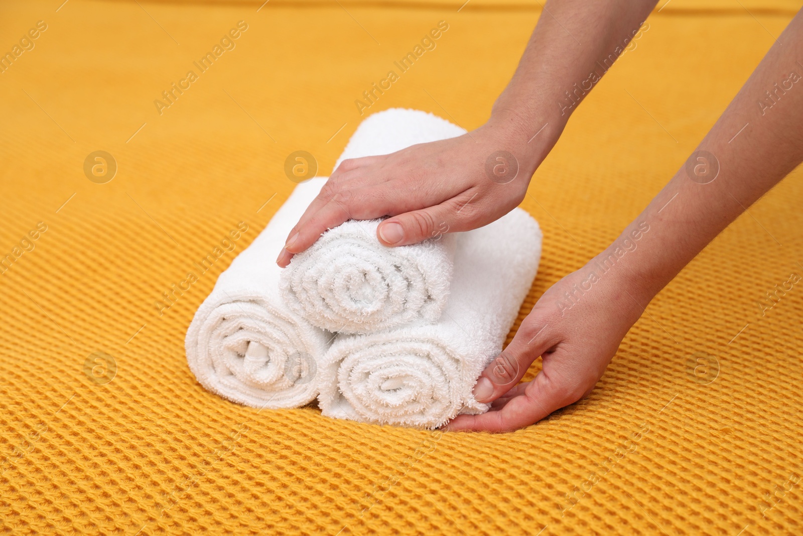 Photo of Woman putting rolled terry towels onto yellow blanket, closeup