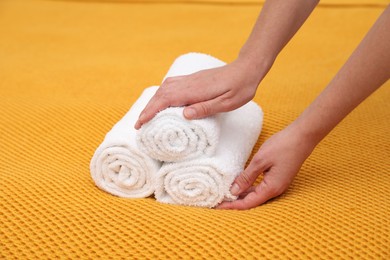 Photo of Woman putting rolled terry towels onto yellow blanket, closeup