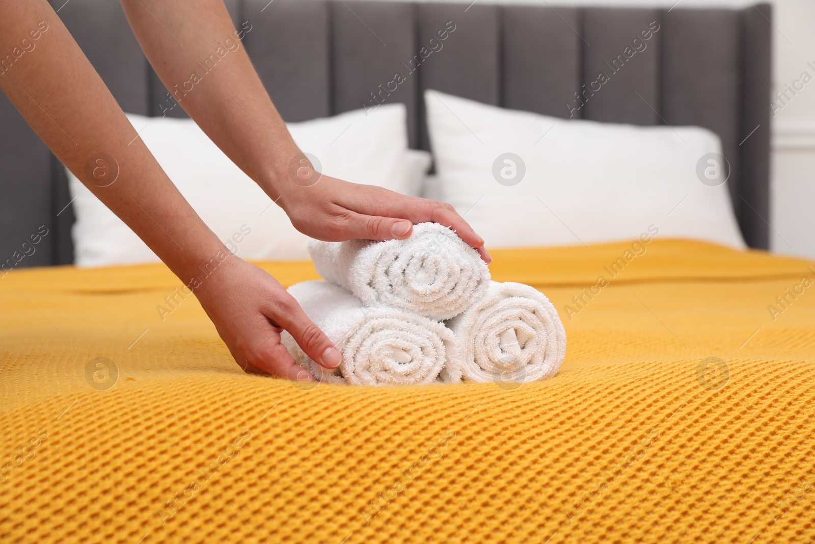 Photo of Woman putting rolled white terry towels onto bed indoors, closeup