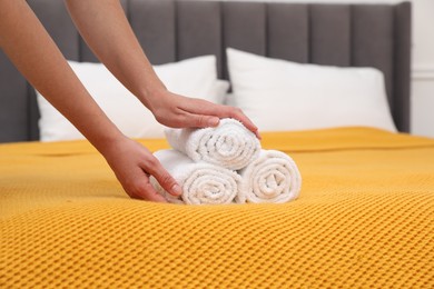 Photo of Woman putting rolled white terry towels onto bed indoors, closeup