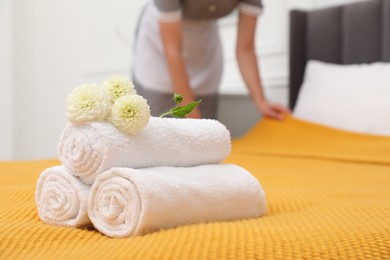 Photo of Chambermaid working in hotel room, focus on rolled terry towels and dahlia flowers on bed
