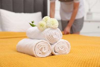 Photo of Chambermaid working in hotel room, focus on rolled terry towels and dahlia flowers on bed