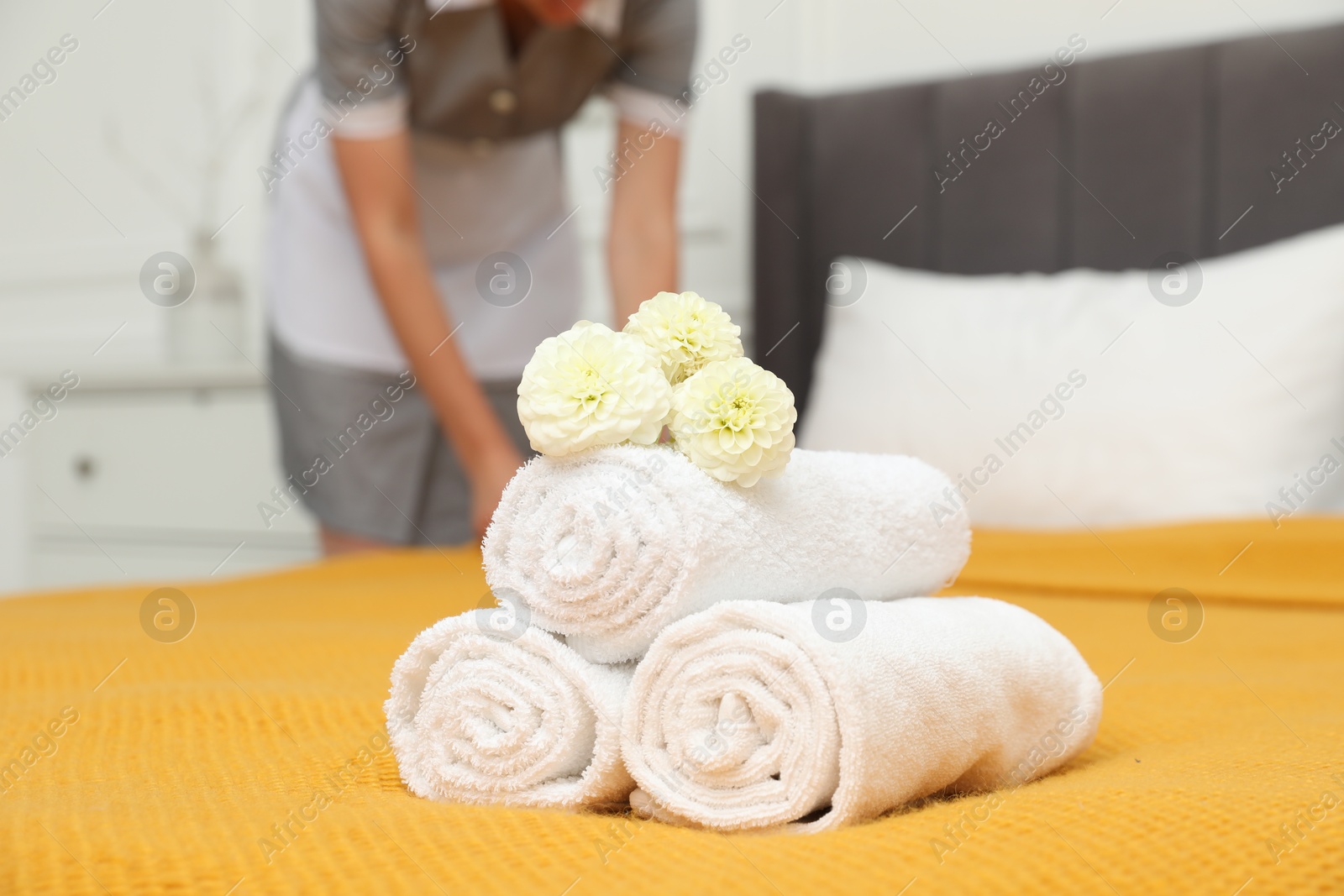Photo of Chambermaid working in hotel room, focus on rolled terry towels and dahlia flowers on bed