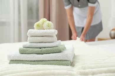 Photo of Chambermaid working in hotel room, focus on stack of terry towels and dahlia flowers on bed