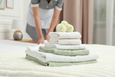 Photo of Chambermaid working in hotel room, focus on stack of terry towels and dahlia flowers on bed