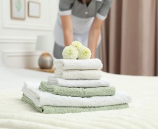 Photo of Chambermaid working in hotel room, focus on stack of terry towels and dahlia flowers on bed