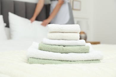 Photo of Chambermaid working in hotel room, focus on stack of terry towels on bed